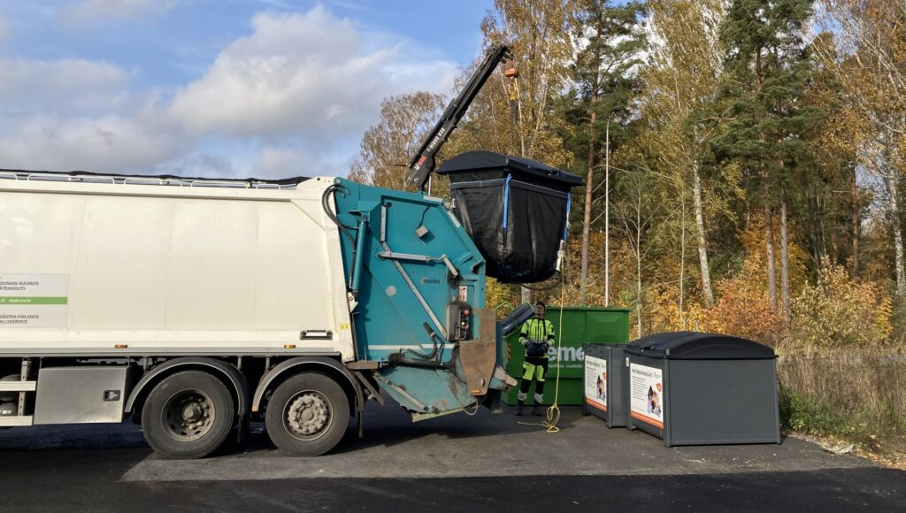 En sopbil med kran tömmer en avfallsbehållare.